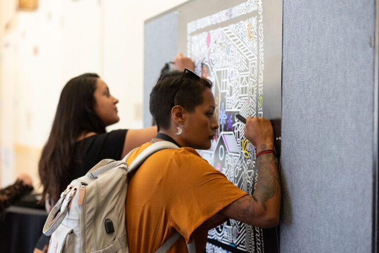 two people use markers to color on a poster hanging on a wall