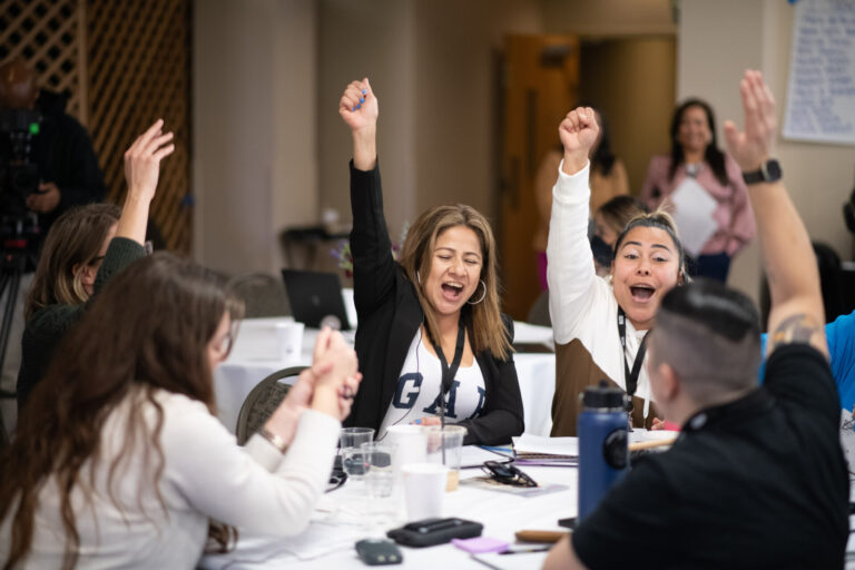 Community leaders in Washington State sitting around a table in a conference room, raising their hands in joy or exclamation