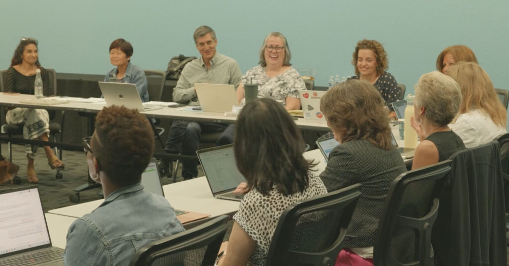 members of SV2's governing board sit around a table with laptops on the desks in front of them