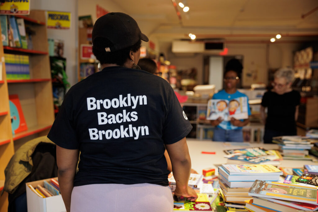 A woman wearing a "Brooklyn Backs Brooklyn" t-shirt sorts books with other volunteers