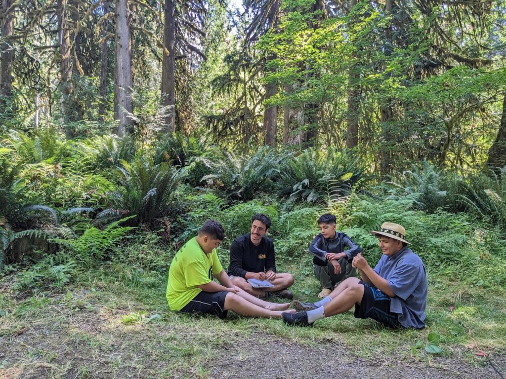 four people sit in a circle in the forest